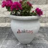 50x50x50 cm boyutlarında, doğal gri beton renginde vazo şeklinde saksı içinde fuşya rengi çiçekli bir bitki ile dış mekanda kullanılmış hali.