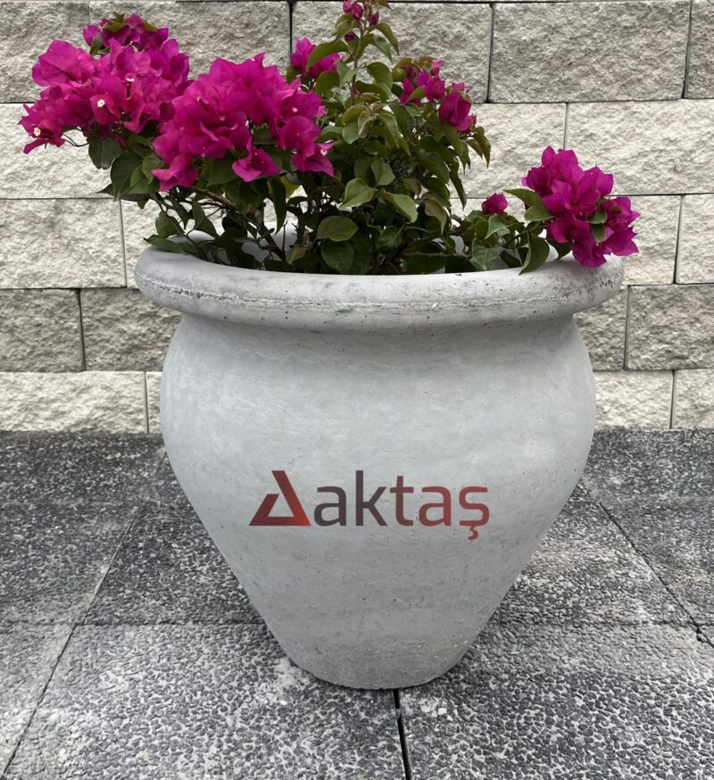 50x50x50 cm boyutlarında, doğal gri beton renginde vazo şeklinde saksı içinde fuşya rengi çiçekli bir bitki ile dış mekanda kullanılmış hali.