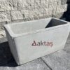 80x40x44 cm boyutlarında, doğal gri renkte pürüzsüz yüzeyli dikdörtgen beton saksı. Bir dış mekan duvarının önünde, taş zemin üzerinde konumlandırılmıştır.
