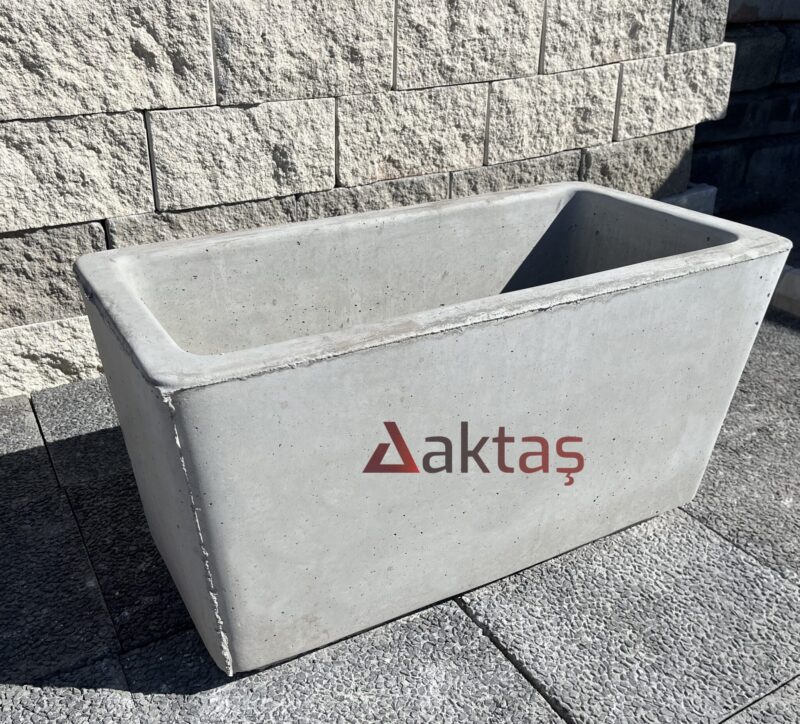 80x40x44 cm boyutlarında, doğal gri renkte pürüzsüz yüzeyli dikdörtgen beton saksı. Bir dış mekan duvarının önünde, taş zemin üzerinde konumlandırılmıştır.