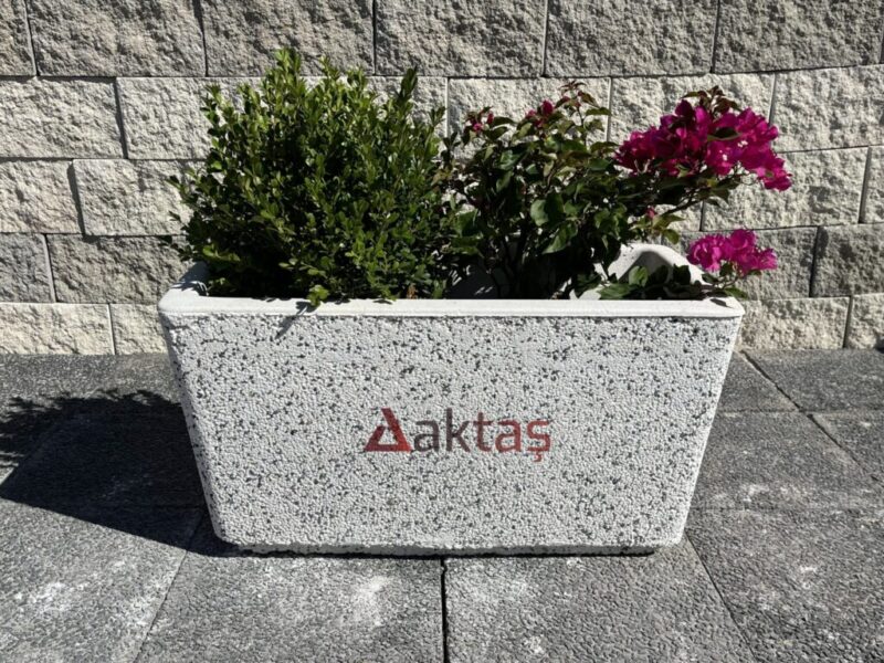 80x40x44 cm boyutlarında, beyaz mozaikli dikdörtgen beton saksı içinde yeşil bitkiler ve pembe çiçekler ile dış mekanda kullanılmış hali.