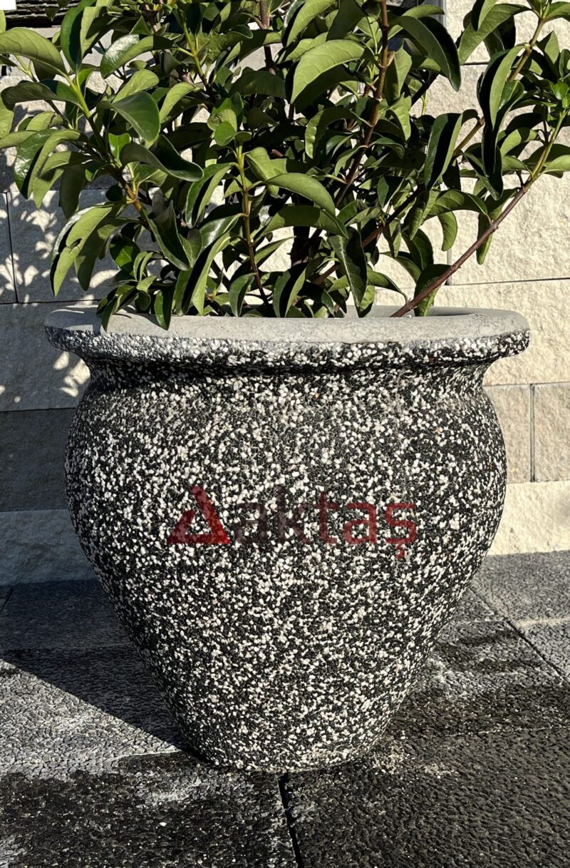 50x50x50 cm boyutlarında, siyah mozaik dokulu vazo şeklinde beton saksı içinde yeşil yapraklı bir bitki ile dış mekanda kullanılmış hali.