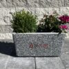Siyah-Mozaikli-Dikdörtgen-Saksı-80x40x44-cm-Aktaş Siyah mozaikli dikdörtgen beton saksı (80x40x44 cm) içinde yeşil bitkiler ve pembe çiçekler ile dış mekanda kullanılmış hali.